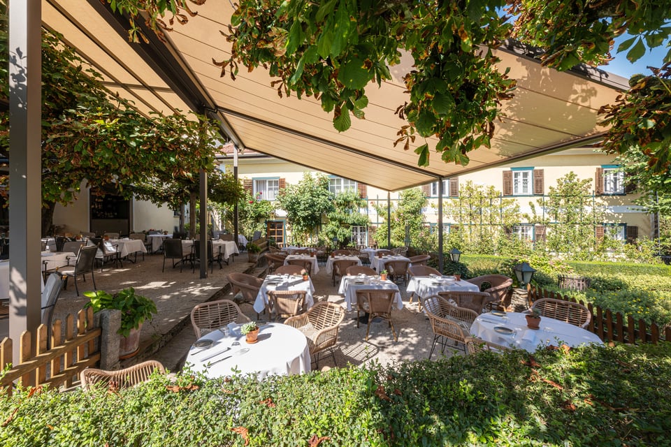 Große markilux pergola stretch überdacht die Gartenterrasse eines Restaurants mit weiß eingedeckten Tischen unter Bäumen.